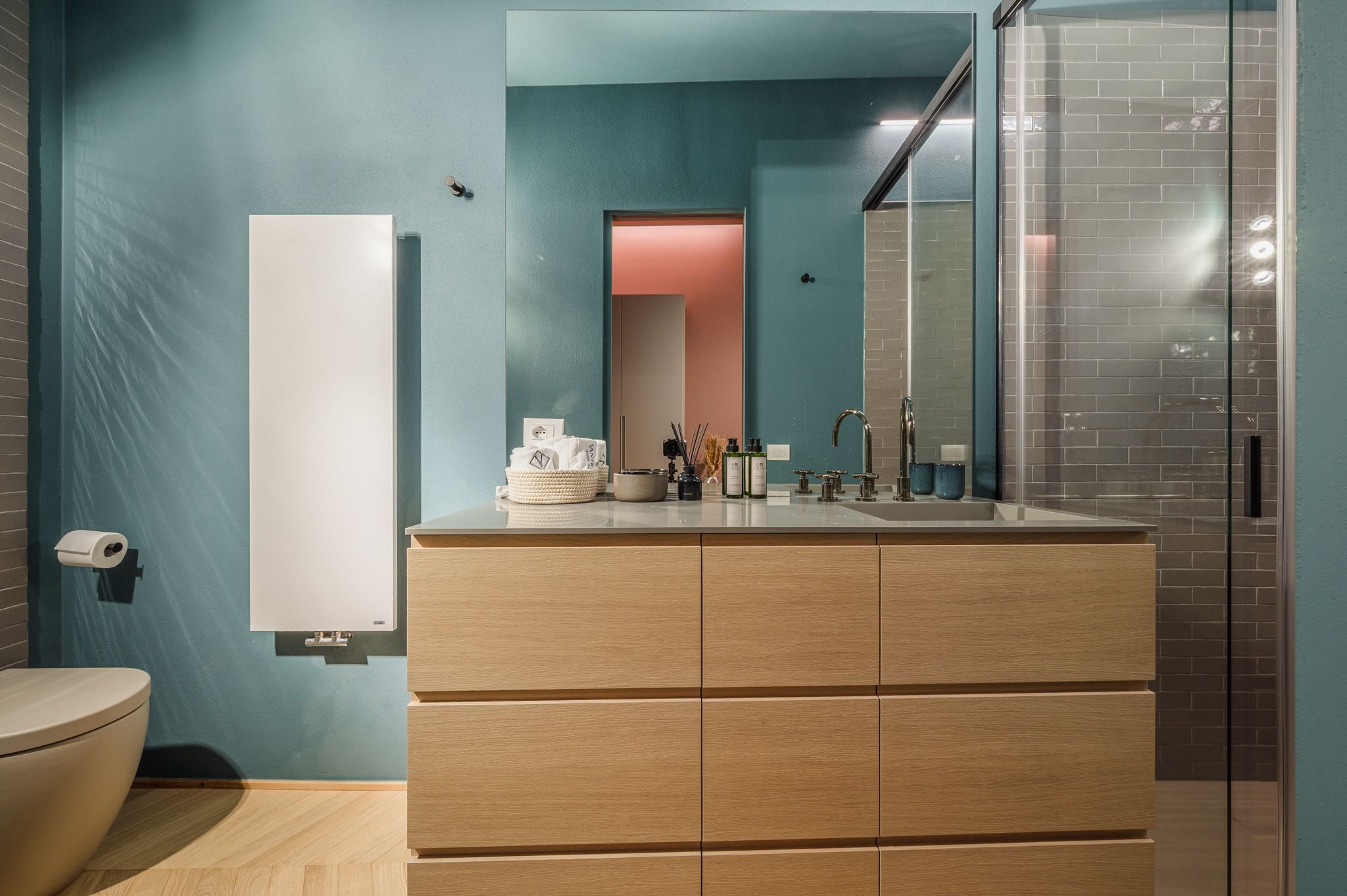 Vanity del bagno turchese con specchio che riflette il bagno rosa sullo sfondo